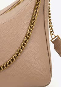 Borsa a mano in pelle beige con superficie testurizzata, dotata di una tracolla in catena dorata e chiusura con zip sulla parte superiore. Forma semplice e angolare.