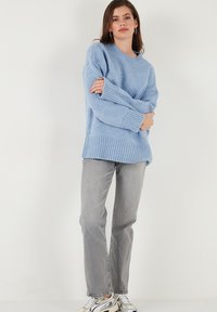 Světle modrý pletený svetr s žebrovaným lemem a manžetami, spárovaný se šedými rovnými džíny a bílými teniskami.