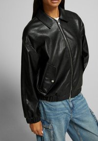 Svart läder bomberjacka med dragkedjestängning, oversized passform och ribbade ärmslut. Har sidofickor och en klassisk krage. Texturerad yta.