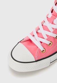 Rózsaszín vászon sneaker fehér fűzőkkel, arany szegecsekkel, gumiborítású orral és fekete díszítéssel. Jellemzője a texturált talp a tapadásért.