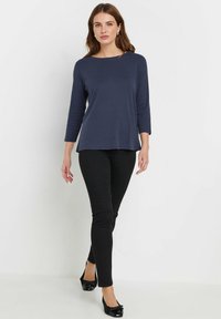 Navyblaues Langarmoberteil mit Bootsausschnitt, kombiniert mit schwarzen engen Hosen und schwarzen Ballerinas, hergestellt aus einem glatten Stoff und im lässigen Schnitt.