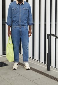 Jeansjacka med en beige krage, matchande jeans och en ljusgrön tote-väska. Bärs med krämfärgade och svarta sneakers på en strukturerad yta.