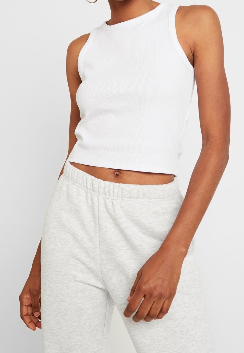 Vit ribbad linne med hög hals och kort passform, i kombination med ljusgrå mjukisbyxor med elastiskt midjeband.