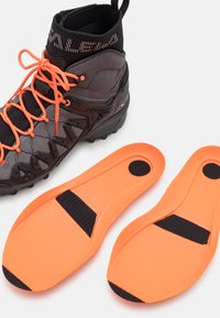 Fottur i mørkegrått med oransje snører og detaljer; inkluderer oransje innersåler med svarte stropper. Teksturert stoff og gummisåle.