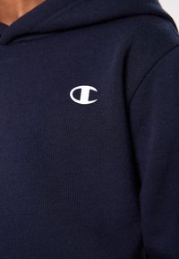 Felpa blu navy realizzata in morbido tessuto, con un piccolo logo bianco sulla parte sinistra del petto e un classico design con cappuccio regolabile.