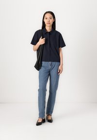 Camisa de manga corta de color navy con cuello, combinada con jeans rectos de color azul claro y zapatos de tacón cuadrado negros, complementados con un bolso tote negro.