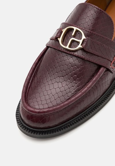 Mocasini din piele burgund cu un model texturat hexagonal, având un accent de cataramă aurie și o talpă ribbată neagră.