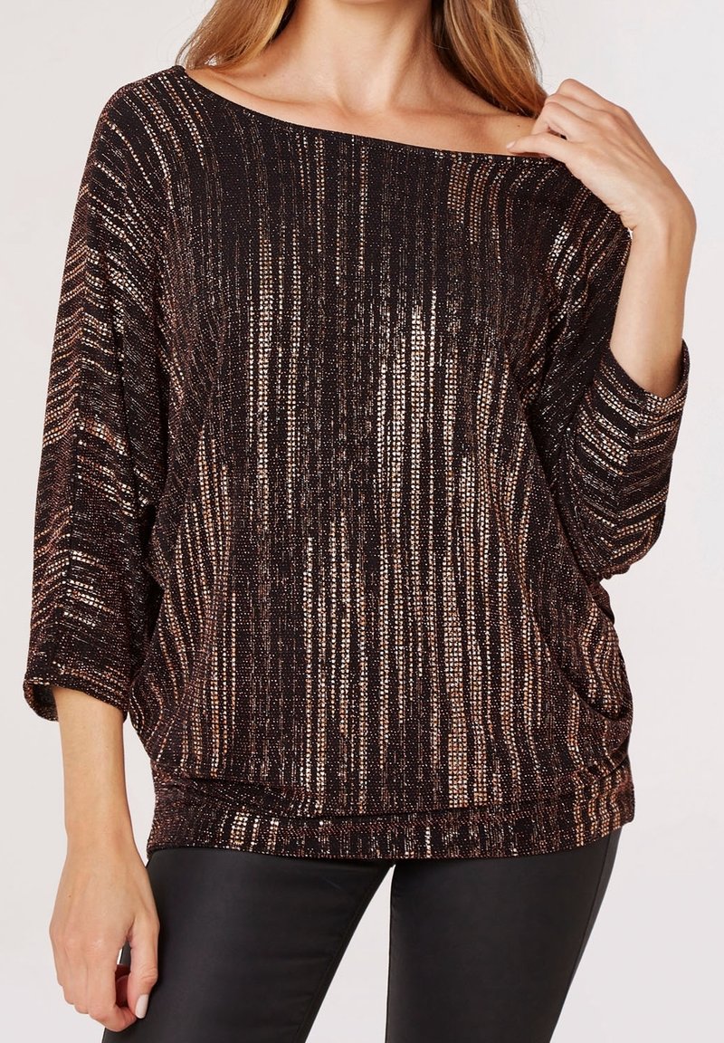 Femme portant un haut ample rayé noir et cuivre à épaules dénudées avec manches trois-quarts et pantalon noir ajusté.