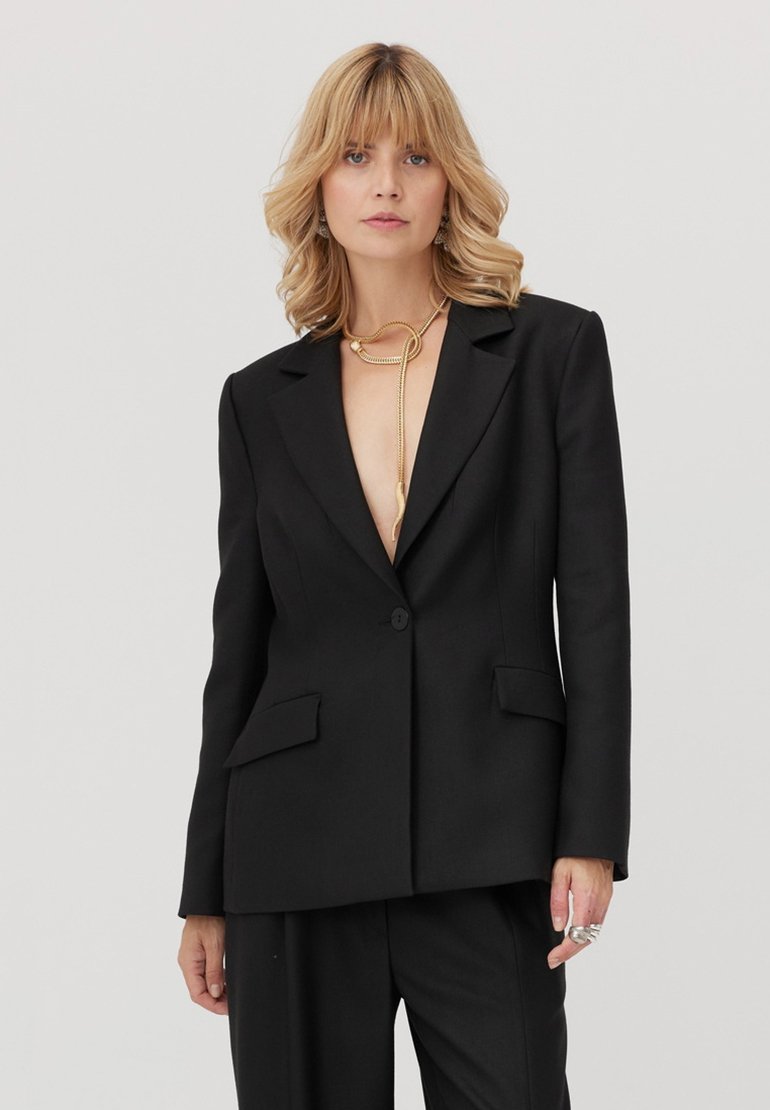 Czarna, dopasowana marynarka z klapą z wcięciem, dwoma przednimi kieszeniami, zamykana na jeden guzik, o luźnym kroju. Materiał wydaje się gładki i strukturalny.