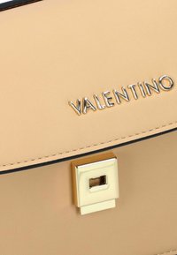 Borsa a mano in pelle beige con chiusura a serratura quadrata dorata e logo impresso. Texture liscia e rifinitura nera a contrasto lungo i bordi.