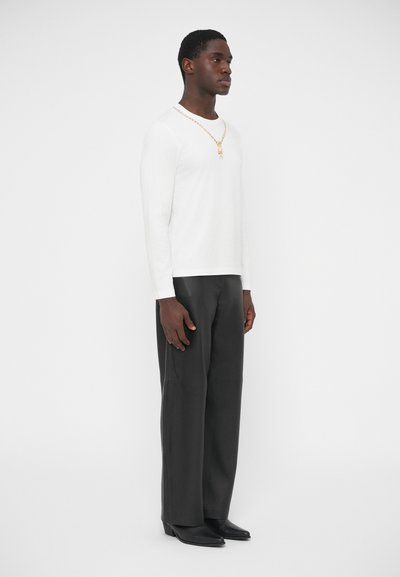 Biela košeľa s dlhým rukávom, tmavé široké nohavice a čierne špicaté topánky. Oblečenie dopĺňa zlatý retiazkový náhrdelník s príveskom.