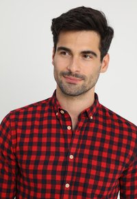 Camisa de cuadros rojos y marinos de botones en algodón, con cuello, tela con estampado y botones en contraste. No hay bolsillo visible.