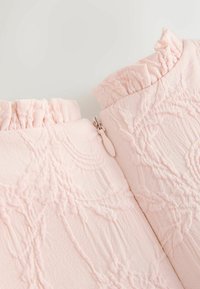 Hellrosa strukturierten Stoff mit Blumenmustern, versehen mit einem gerafften Kragen und einem kleinen zentralen Reißverschlusszug.