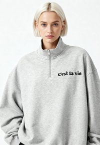 Grijs quarter-zip sweatshirt met een zachte textuur, een comfortabele pasvorm en zwarte opdruk met de tekst "c'est la vie" op de voorkant.