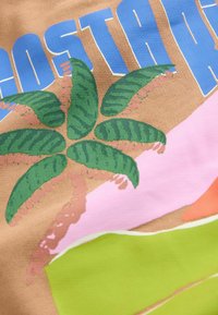 Vaaleanruskea kangas, jossa on sininen "COSTA RICA" -teksti. Taustalla vihreä palmukuvio ja vaaleanpunaisia, oransseja sekä vihreitä abstrakteja muotoja.
