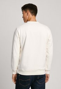 Mikina s kulatým výstřihem v barvě off-white z měkké bavlny, s jemnou texturou, žebrovanými manžetami a lemem, a uvolněným střihem. V kombinaci s tmavými džíny.