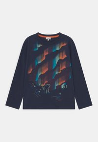 Navy pitkähihainen paita, jossa on värikkäät revontulet, hiihtäjiä otsalamppujen kanssa ja suuri hohtava olento lähellä mökkiä.