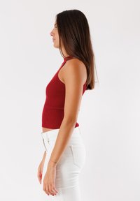 Top in maglia rossa a coste con scollatura alta, abbinato a jeans bianchi aderenti. Il top ha un design corto, che enfatizza una silhouette snella.