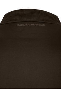 Tummanruskea teksturoitu kaulus, jossa on "KARL LAGERFELD" -logo painettuna sileälle kankaalle kaularoikkuun alle.