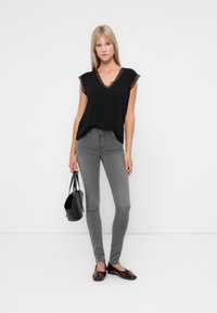 Top negro de manga corta con encaje, combinado con jeans ajustados grises y bailarinas burdeos. La modelo sostiene un pequeño bolso negro.