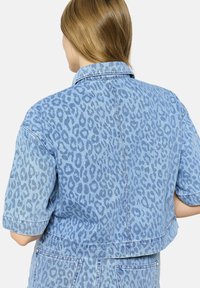 Krátka džínsová bunda v svetlomodrej farbe s leopardím vzorom. Má krátke rukávy a klasický golier. Mäkčená, textúrovaná látka.