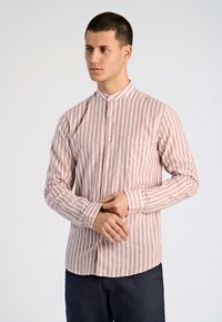 Camicia a righe in rosso chiaro e crema; presenta un colletto a fascia, maniche lunghe e una tasca sul petto; il tessuto appare leggero.