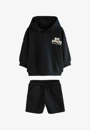 Sweat-shirt à capuche noir avec le texte « Big Smiles All Day Everyday » sur la poitrine, assorti à un short noir à taille élastique avec cordon de serrage et poches.