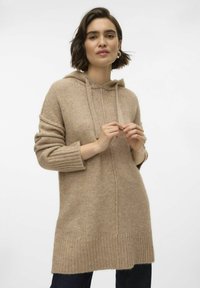 Pulover cu glugă tricotat bej, cu manșete și tiv răsfrânte, țesătură texturată și șnur frontal. Modelul își ține mâinile aproape de centrul corpului.