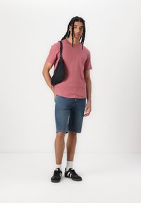 Rdeča majica s kratkimi rokavi, denim kratke hlače, črna torbica čez telo in črne superge z belimi detajli. Enostavna podlaga.