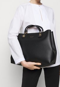 Sac à main en cuir noir avec une surface texturée, deux anses supérieures et des accents en métal doré. Design compact avec une base légèrement large.