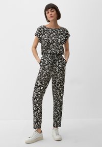 Ensemble coordonné en imprimé léopard noir et blanc comprenant un haut à manches courtes et un pantalon fuselé avec poches, complété par des sneakers blanches.