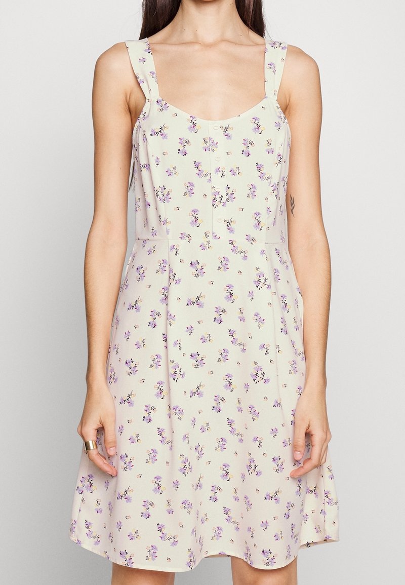 Robe à motif floral jaune clair avec des fleurs violettes, dotée d'un décolleté arrondi, de fines bretelles et d'une jupe évasée.