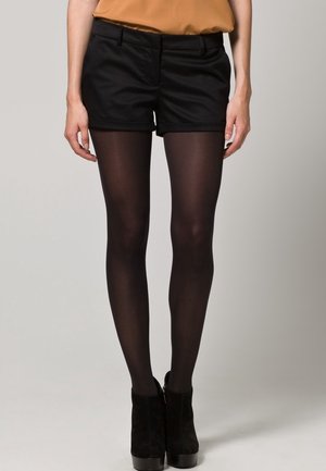 Zwarte op maat gemaakte shorts met een gladde textuur, gecombineerd met doorzichtige zwarte panty’s en zwarte hoge laarzen, creëren een eigentijdse look.