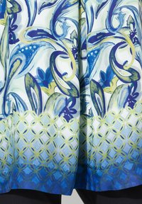 Multifarvet bluse med et blomster- og paisleymønster i blå, grøn og hvid, samt et geometrisk mønster i gul og blå i bunden.