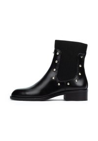 Botín negro de cuero con parte superior de tela ribeteada. Presenta tachuelas doradas a lo largo de los laterales y un tacón bajo. Textura suave y diseño elegante.