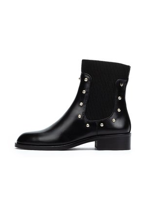 Botín negro de cuero con parte superior de tela ribeteada. Presenta tachuelas doradas a lo largo de los laterales y un tacón bajo. Textura suave y diseño elegante.