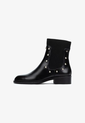 Bottines noires en cuir avec un uppers en tissu côtelé. Présente des clous dorés sur les côtés et un petit talon bloc. Texture lisse et design élégant.
