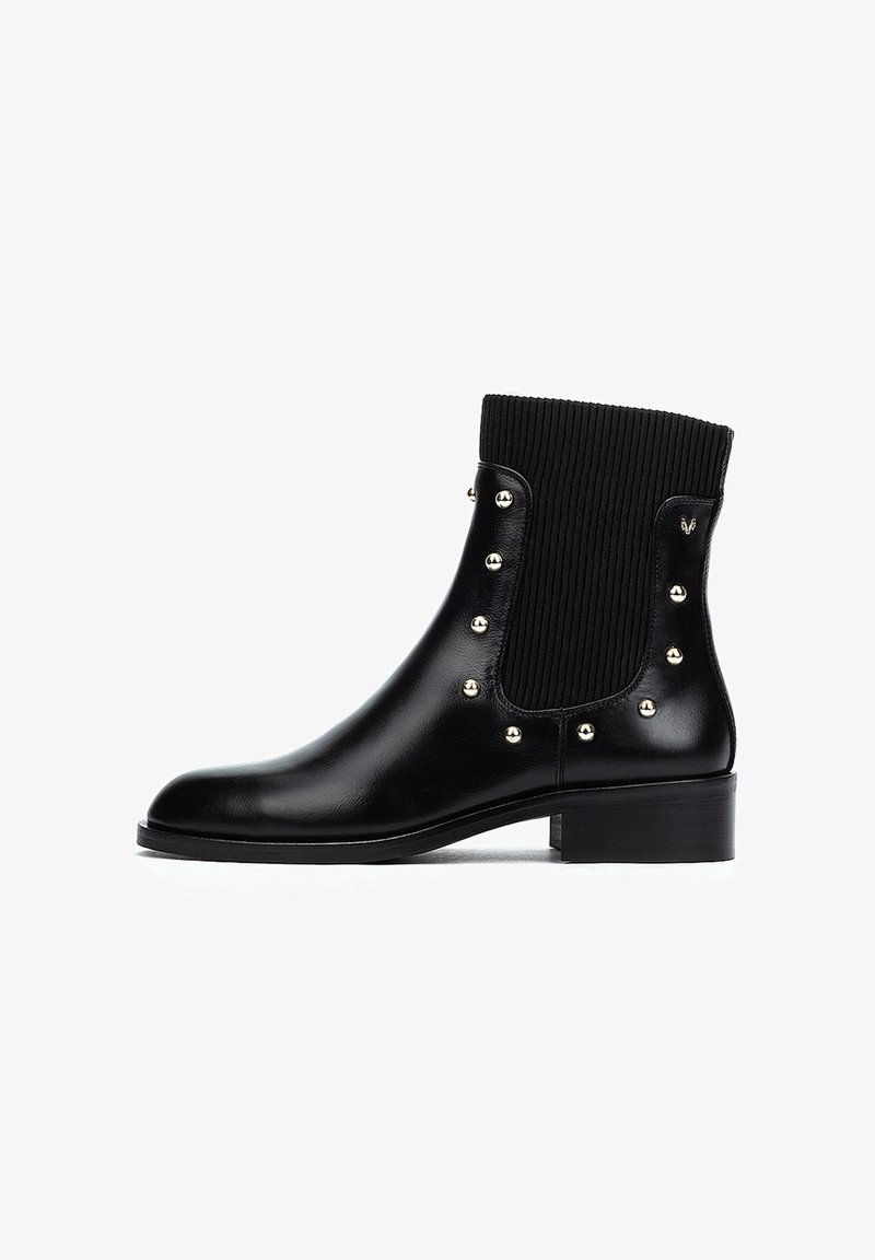 Botín negro de cuero con parte superior de tela ribeteada. Presenta tachuelas doradas a lo largo de los laterales y un tacón bajo. Textura suave y diseño elegante.
