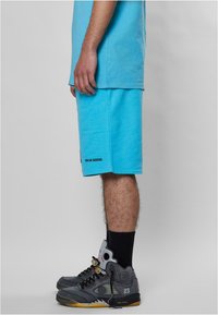 Lyseblå bomull T-skjorte parret med matchende shorts. Merkbar merkevare på shortsene: "SENSE." Grå sneakers med svarte detaljer og synlig luftdemping.