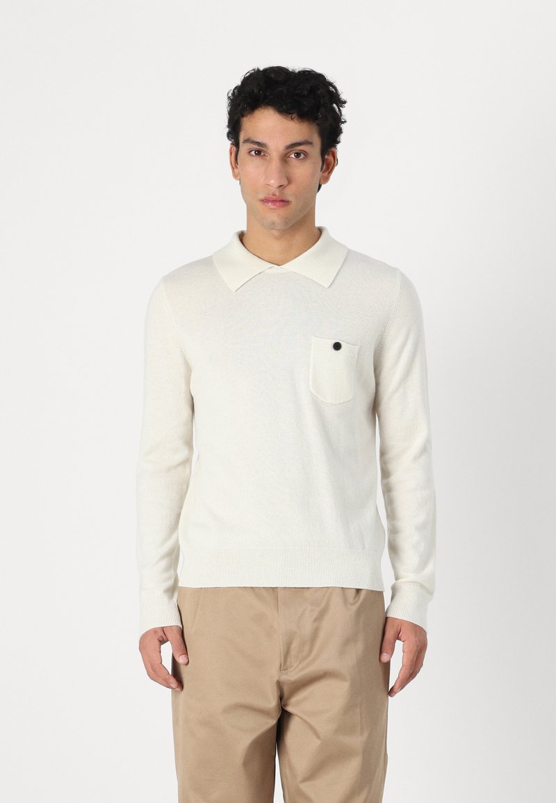 Pulôver de malha de cor creme com colarinho tipo polo, mangas longas e um bolso no peito com um botão preto. Tecido texturizado, design ajustado.