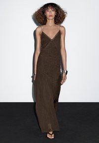 Brown, textured maxi dress with thin straps and a V-neck. Features a gathered design and a flowing silhouette, paired with black sandals.