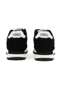 Schwarze Wildleder-Sneaker mit weißen Akzenten, versehen mit der Zahl "1968" an der Ferse. Dicke Gummisohle für Grip und Komfort.