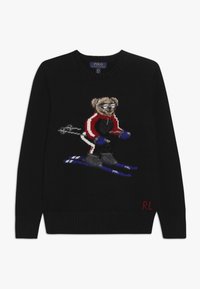 Svart stickad tröja med en skidande björnmotiv i röd och blå sportklädsel. Inkluderar broderade detaljer och ribbade ärmslut.