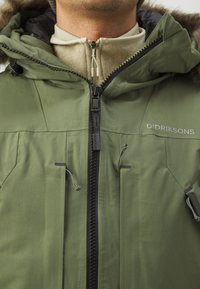 Giacca verde resistente alle intemperie con chiusura a zip, cappuccio regolabile e numerose tasche, realizzata in tessuto resistente con una finitura strutturata.
