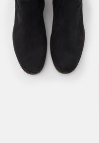 Botines de ante negro con una textura suave, punta redonda, paneles laterales elásticos y detalles de suela marrón cosidos.