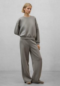 Felpa grigia e pantaloni larghi. Tessuto morbido, vestibilità rilassata, polsini e vita a coste. Dettagli di cucitura distintivi e design minimale.