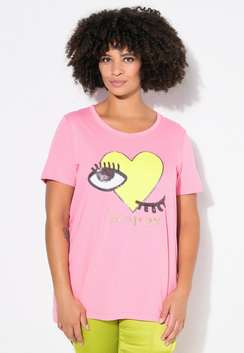 Camiseta de algodón rosa con un gráfico de un corazón amarillo con un ojo, pestañas negras y la palabra "Feliz" en glitter dorado debajo del diseño.