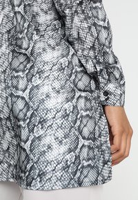 Camicia a stampa serpente in bianco e nero con maniche lunghe e polsini abbottonati, caratterizzata da una superficie testurizzata che ricorda le scaglie di rettile.