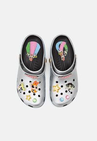 Sabots en plastique argenté avec des trous de drainage noirs, décorés d'autocollants colorés de personnages et d'accents étoiles sur la surface supérieure.