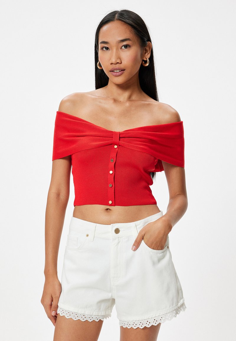 Rød off-shoulder crop top med ribbet tekstur og frontlukning med knapper, parret med hvide shorts med hulmønster i kanten og lommer.